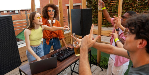 A group of people partying and enjoying outdoors music , while a DJ plays the music aided with powerful outdoor speakers.