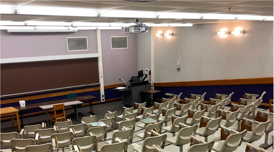 Modern lecture hall with rows of empty chairs, projector, ceiling lights and digital podium setup for interactive teaching