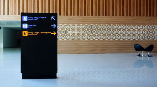 Digital signage display in a modern hotel lobby showing directional guidance with illuminated arrows and icons