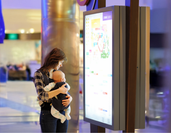 Woman holding baby using digital signage display in public space for informational messaging