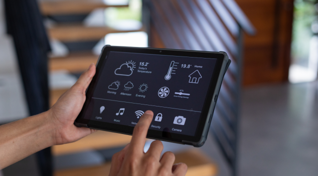Close-up of person controlling smart home functions on a touchscreen tablet, adjusting lights, temperature, and security