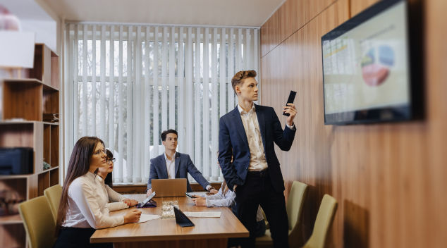 Business professionals in a hotel meeting room using conferencing tools with a wall mounted screen and video call setup