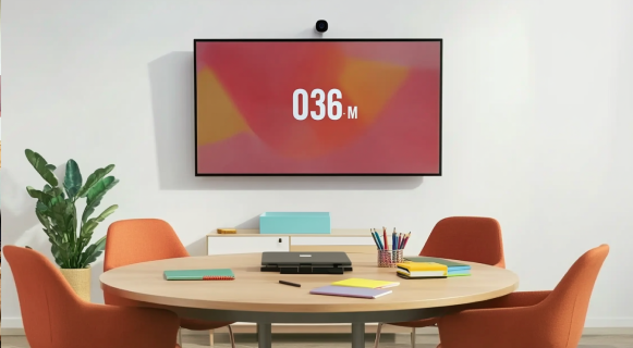 Small meeting room with round table, display screen, camera, and video conferencing setup.