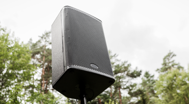 Weatherproof speaker set up outdoors, surrounded by trees under cloudy sky