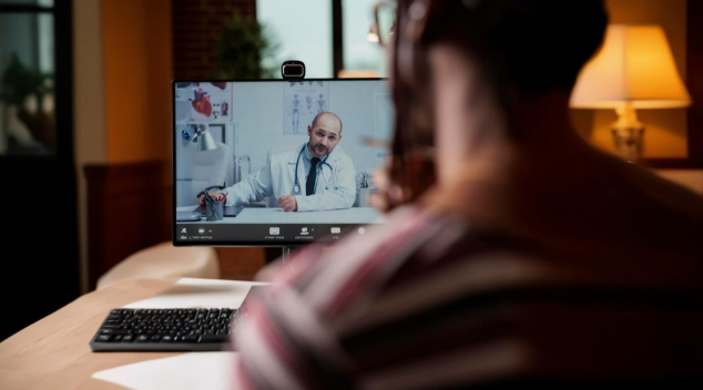 Patient in a home setting consulting with a doctor through a video call on a desktop computer with webcam