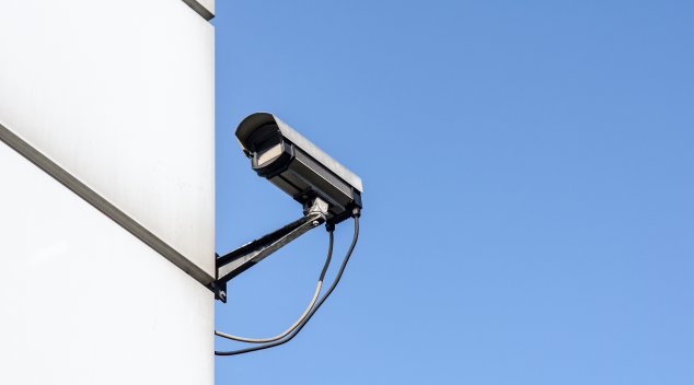 Outdoor security camera mounted on modern building wall against a clear blue sky