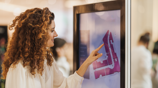 Woman using a digital wayfinding kiosk in a shopping mall to navigate store locations on an interactive map