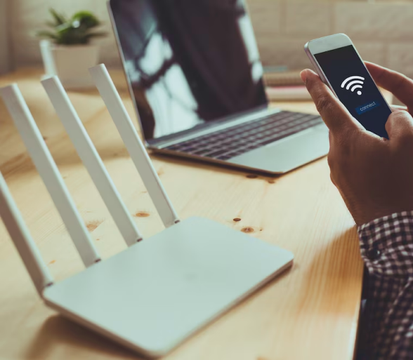 Person connecting smartphone to enterprise-grade Wi-Fi router with laptop on desk in modern office