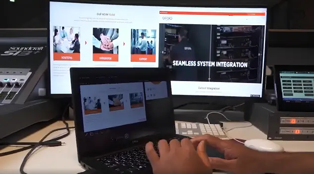 Oxford Integration team member working on a laptop connected to a large monitor displaying a system integration website with multiple sections and images.