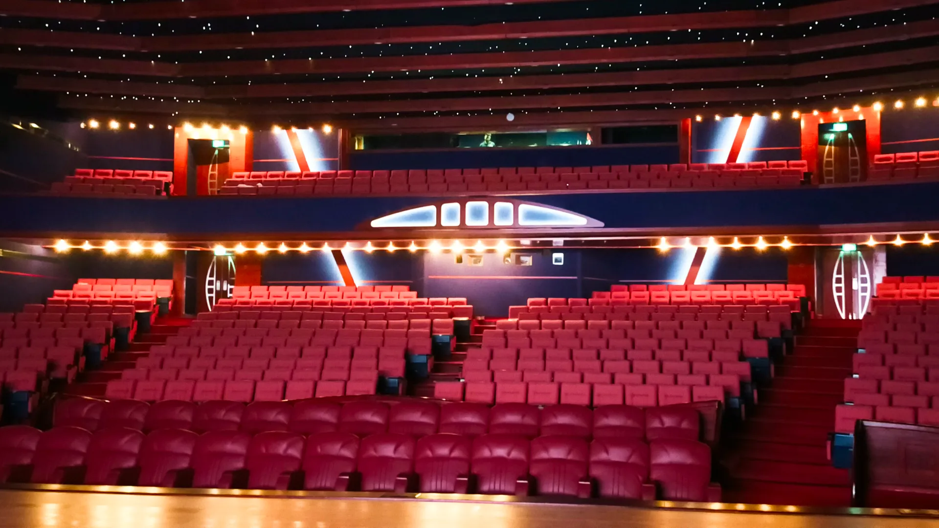 Wide interior view of the Al Ain Municipality auditorium featuring red seating balconies and architectural house lighting integrated by Oxford Integration