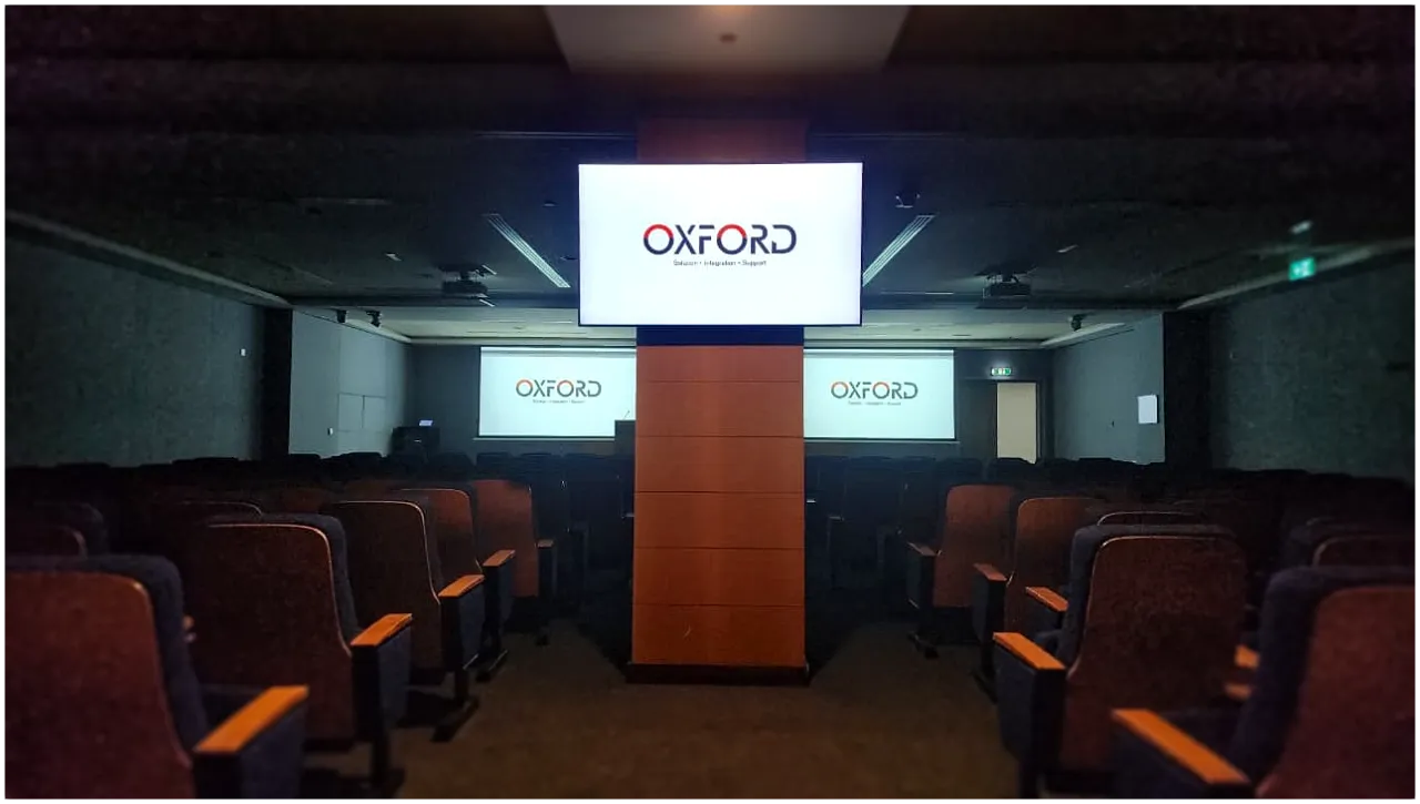 Auditorium view showing Oxford Integration’s projection and display setup with ceiling mounted projectors and central screen.